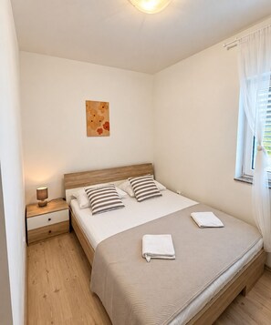 A bedroom with a wooden bed, two bedside tables, a night lamp, a wall art piece, and a window with curtains.
