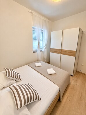 A bedroom with a bed, pillows, a wardrobe, and a window with curtains.