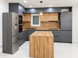 A modern kitchen with a stainless steel refrigerator, wooden cabinetry, a central island, and a pendant light.