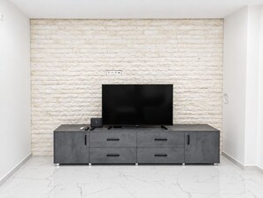 A modern living room with a flat-screen TV on a grey cabinet, a white brick wall, and a marble floor.
