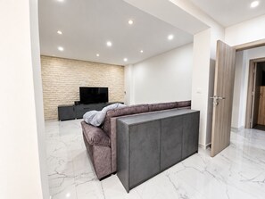 A modern living room with a sofa, entertainment unit, and a television against a stone wall.