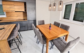 A modern kitchen with wooden cabinetry, a dining table with grey upholstered chairs, and pendant lighting.