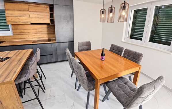 A modern kitchen with wooden cabinetry, a dining table with grey upholstered chairs, and pendant lighting.