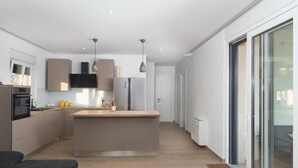 A modern kitchen with a central island, built-in appliances, pendant lighting, and a sliding glass door leading to a balcony. - Beautiful Villa Aria (Zadar)