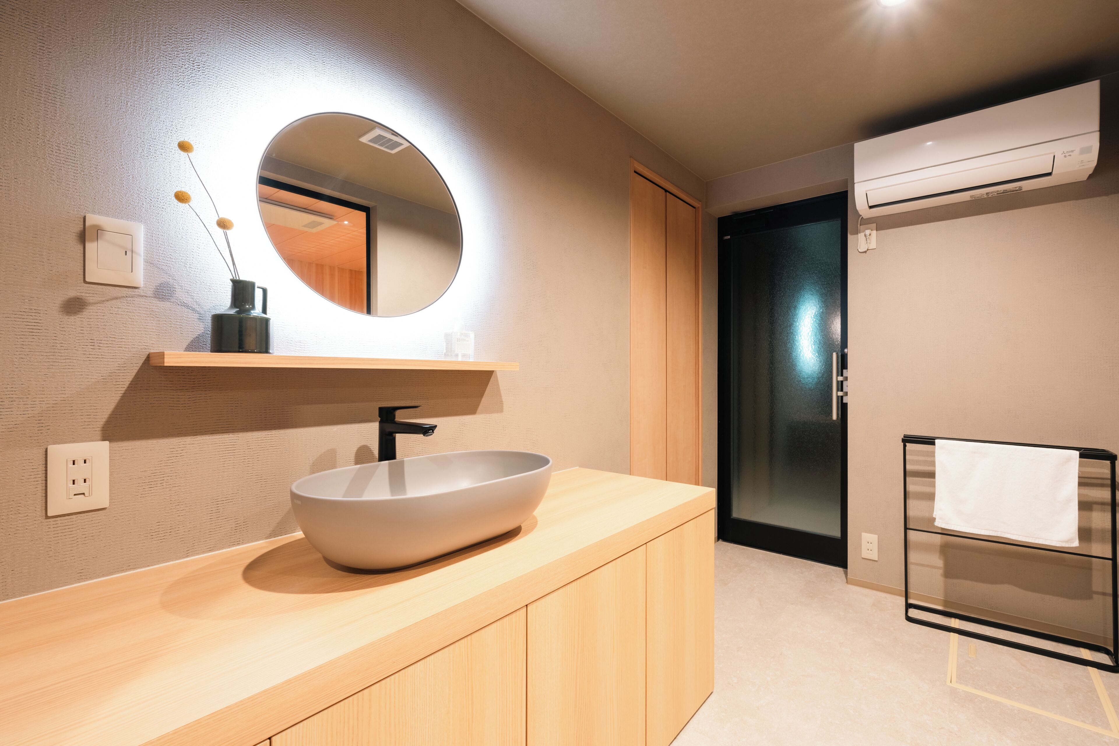 Un baño moderno con un espejo redondo, un lavabo, armarios de madera, un perchero y un equipo de aire acondicionado.