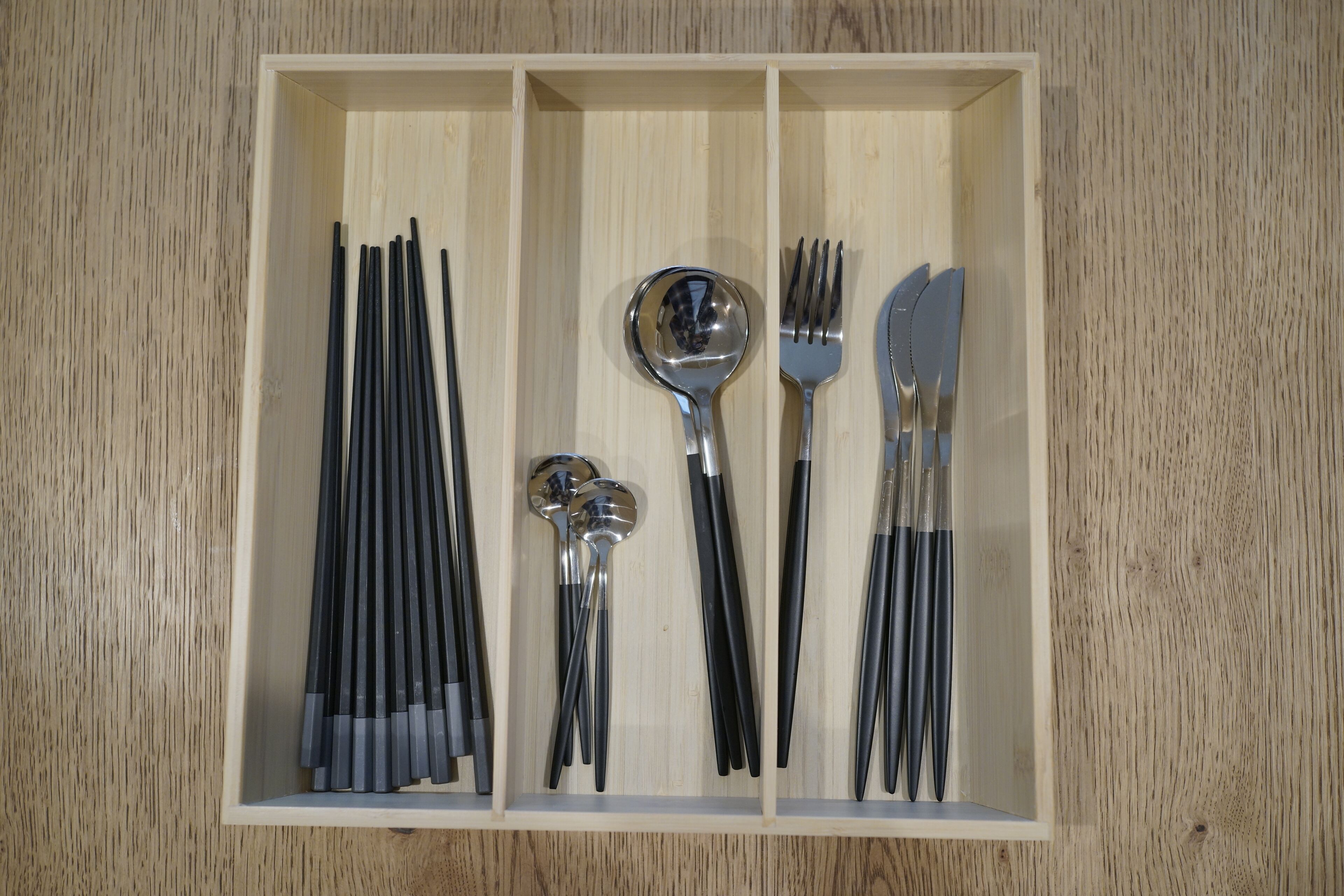Een houten lade met diverse keukengerei er netjes in gerangschikt.
