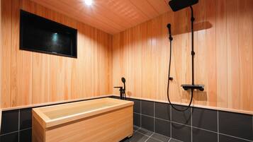 A modern bathroom with wooden panel walls, a wooden bathtub, black tiled flooring, and a mounted television.