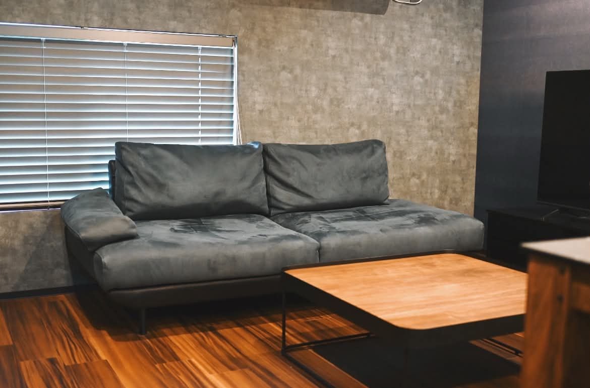 Un salon moderne avec un canapé gris, une table basse en bois et une fenêtre équipée de stores.
