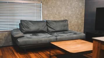 Un salon moderne avec un canapé gris, une table basse en bois et une fenêtre équipée de stores.