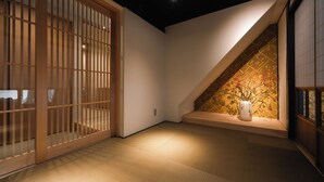Een traditioneel Japans interieur met schuifdeuren, een houten vloer en een klein nisje met een vaas en takken.