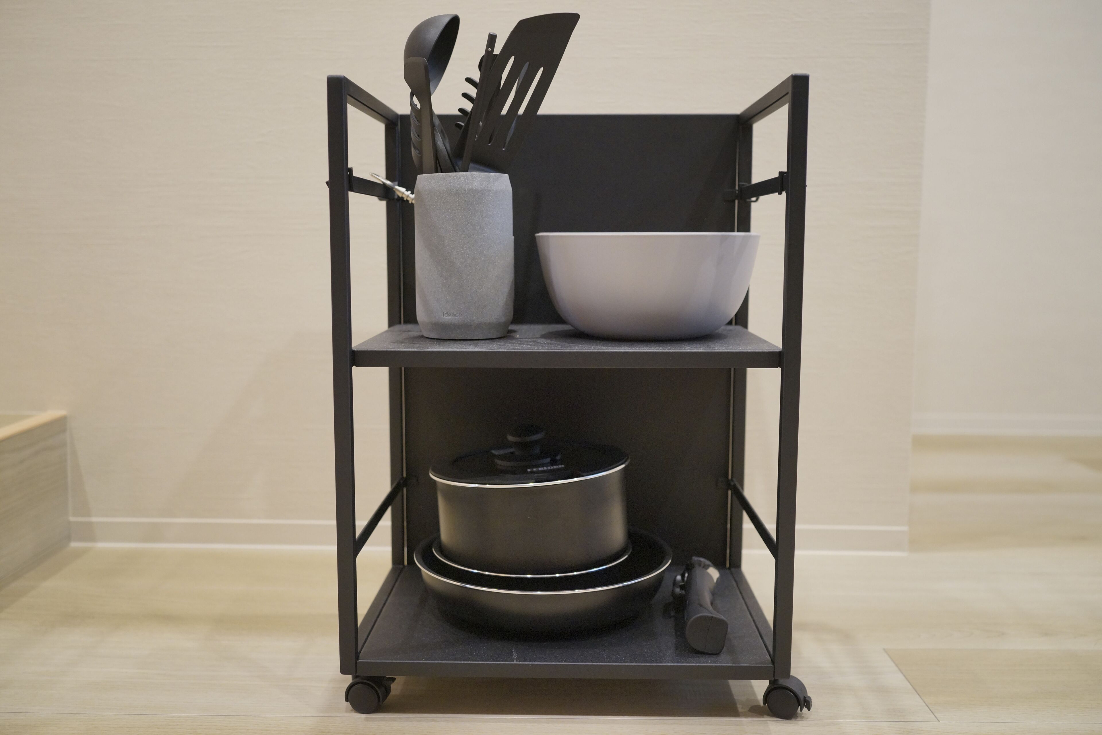 A kitchen cart with a pot, a bowl, and a container holding utensils.