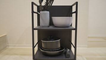 A kitchen cart with a pot, a bowl, and a container holding utensils.