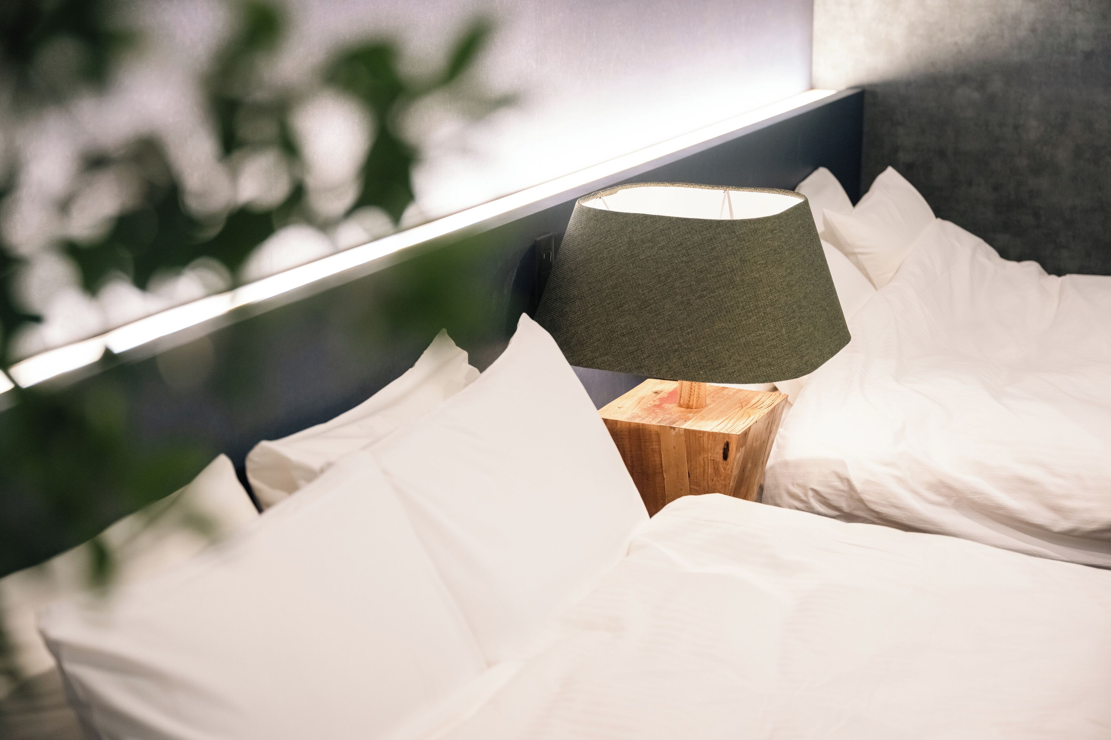 Una cama bien hecha con sábanas blancas y una mesita de noche de madera a un lado.
