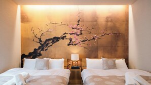 Habitación de hotel con dos camas, cabecera de madera, mesita de noche con lámpara y un cuadro en la pared de una rama con flores rosadas.