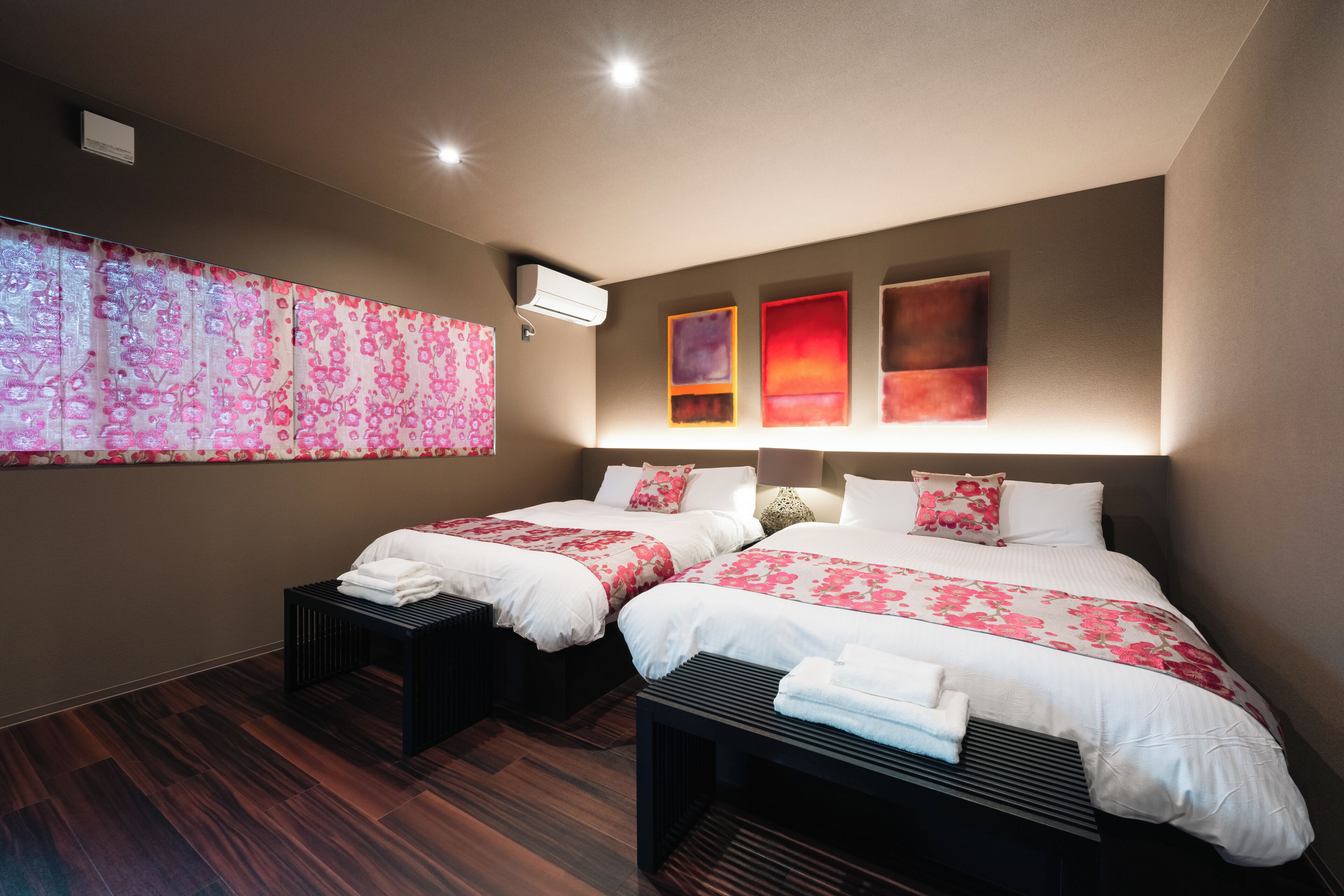 A hotel room with two beds, a large window with a floral view, and artwork on the wall.