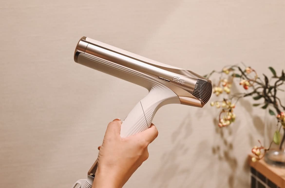 A hand holding a hairdryer with a metallic nozzle and a white handle.