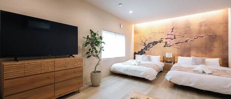 A modern hotel room with a large flat-screen TV, two beds, a wooden dresser, a potted plant, and a wall-mounted artwork.