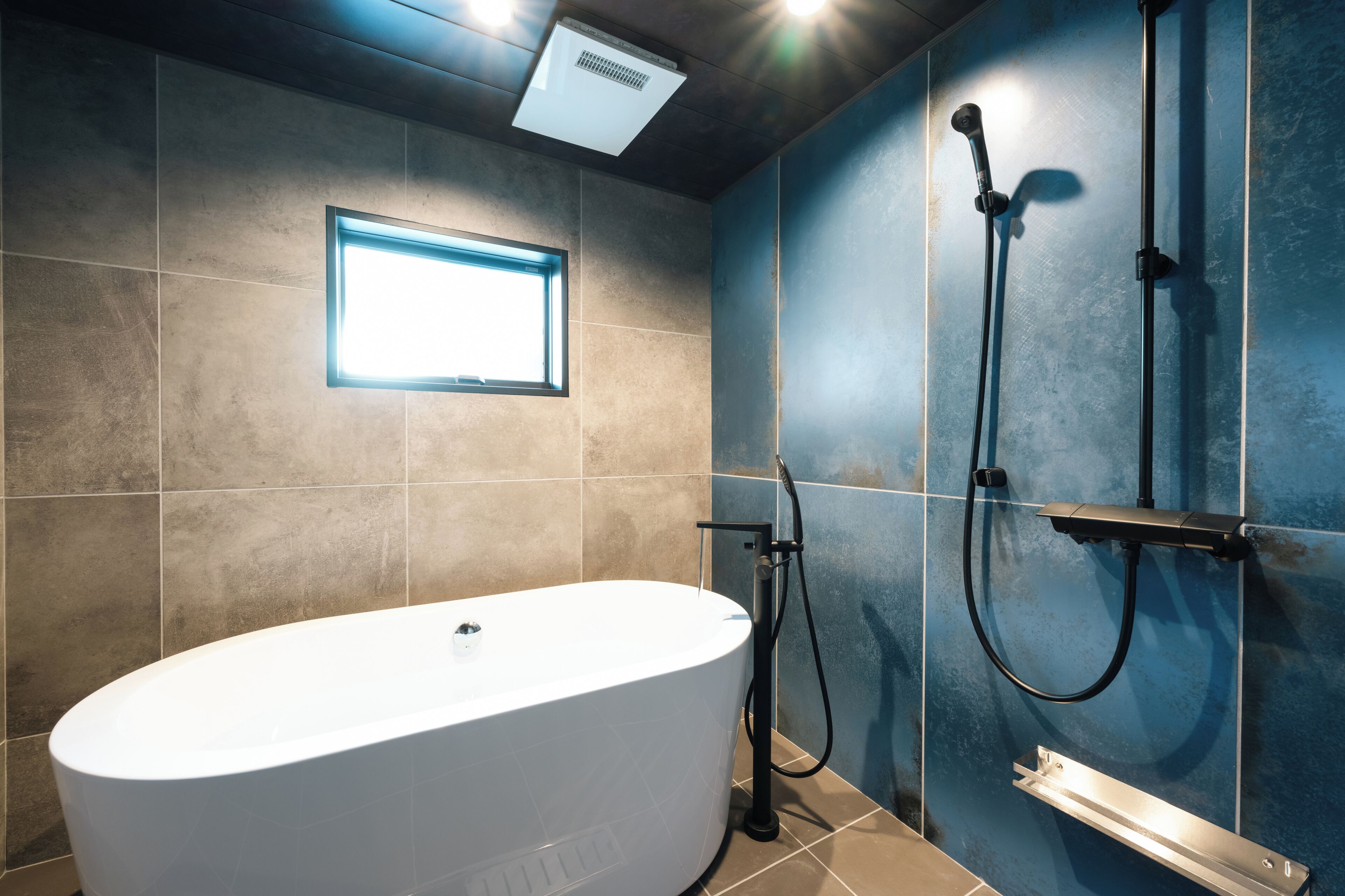 Un baño moderno con una bañera independiente, ducha con cabezal de ducha manual y ventana que proporciona luz natural.