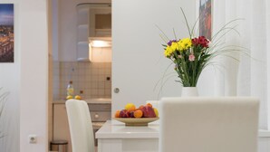 A dining area with a white table, chairs, a vase with flowers, and a fruit bowl.
