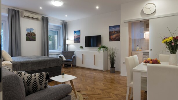 A modern living room with a sofa, a dining table with fruit, a TV, and artwork on the walls.