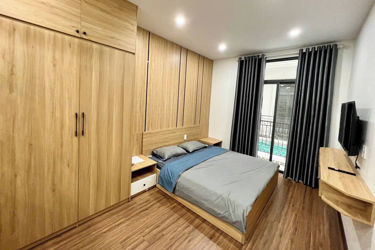 A bedroom with a bed, wooden wardrobe, bedside tables, a TV, and a balcony view.