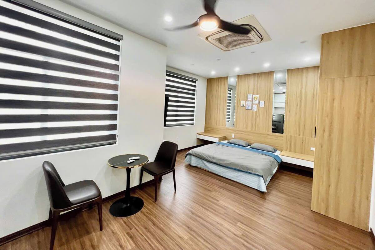 A modern bedroom with a bed, two chairs, a small table, and a ceiling fan.