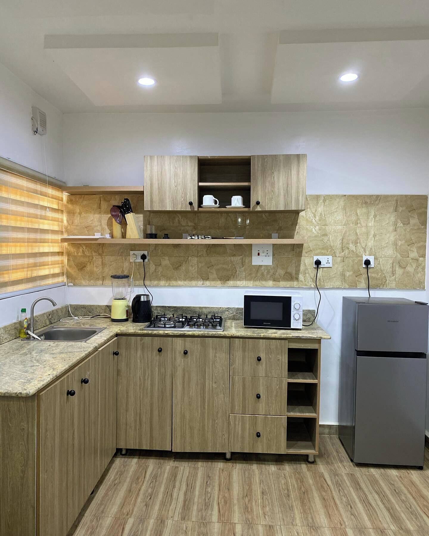 Une cuisine avec des meubles de rangement en bois, un four à micro-ondes encastré, une cuisinière à gaz et un réfrigérateur.