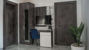 A compact room with a built-in TV, a small white desk, a blue chair, and a potted plant. - Cee- Jackson Apartment  (Benin City)