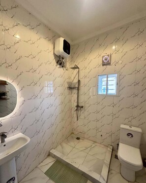 A bathroom with a shower, toilet, sink, and a window. - Softlife Apartments  (Abuja)
