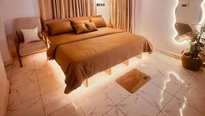 A modern bedroom with a bed, curtains, a chair, and a potted plant. - Softlife Apartments  (Abuja)