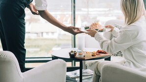 A person in a white shirt and black vest serving food to another person in a white sweater. - Kiviks Hotell Konferens och Spa (Kivik)