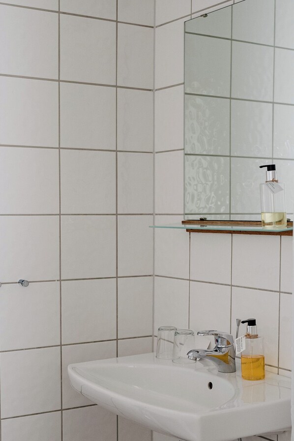 A bathroom with a white sink, a glass shelf with a bottle, and a mirror.