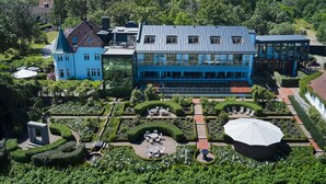 A large, modern building with multiple floors and a glass facade, surrounded by well-maintained gardens and a clear view of the surrounding forest. - Kiviks Hotell Konferens och Spa (Kivik)
