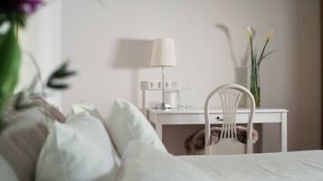 A neatly made bed with white linens, a white desk with a lamp, and a chair with a fur throw.