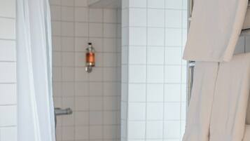 A modern bathroom with white tiles, a shower with a glass door, a towel rack, and a bottle of shampoo.