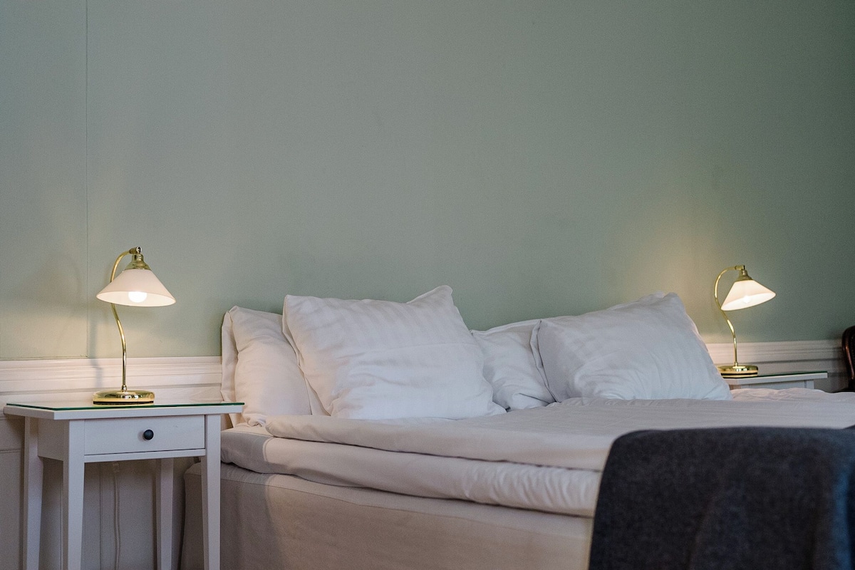A neatly made bed with white linens, two bedside tables with lamps, and a light green wall.