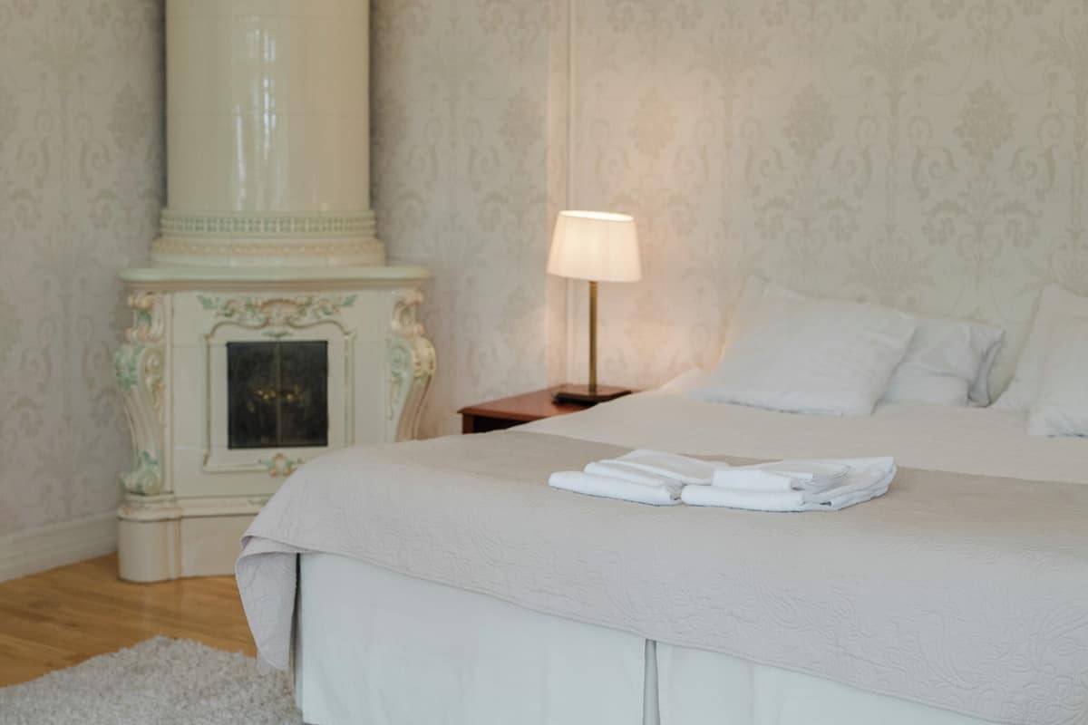 A neatly made bed with a folded towel, a bedside lamp, and a decorative fireplace in a hotel room.