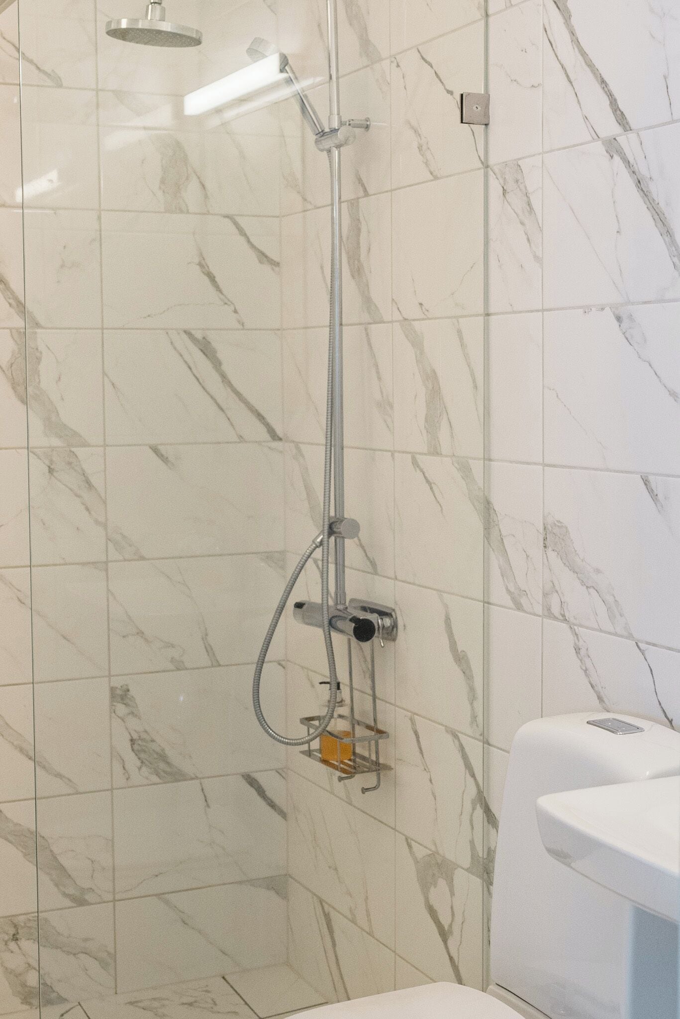 Baño con ducha, azulejos de mármol y lavamanos blanco.