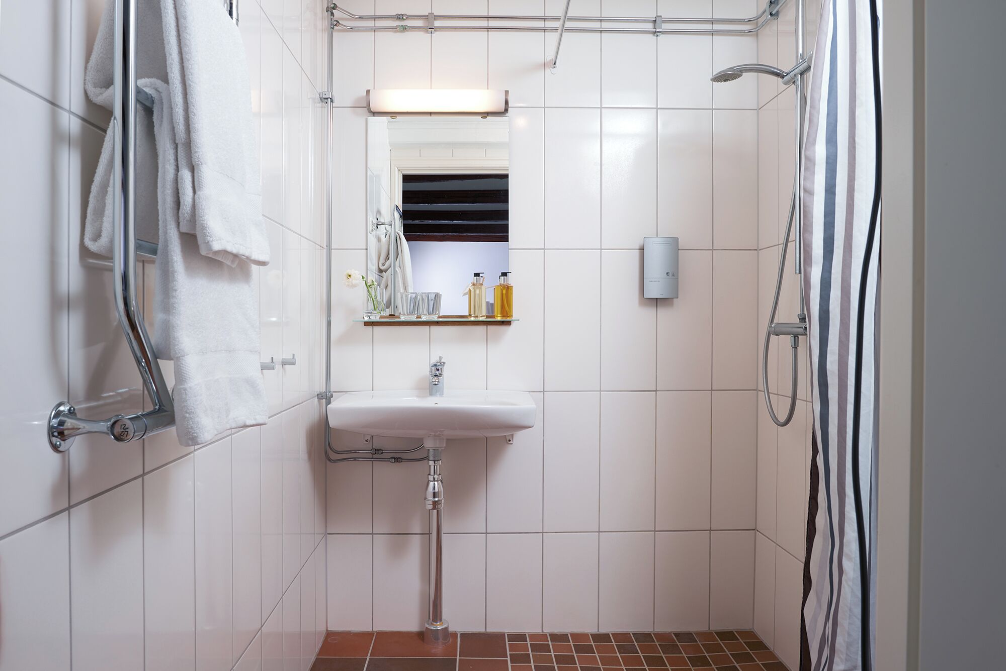 Un baño pequeño y moderno con azulejos blancos, cabina de ducha de vidrio, lavabo blanco y espejo sobre él.