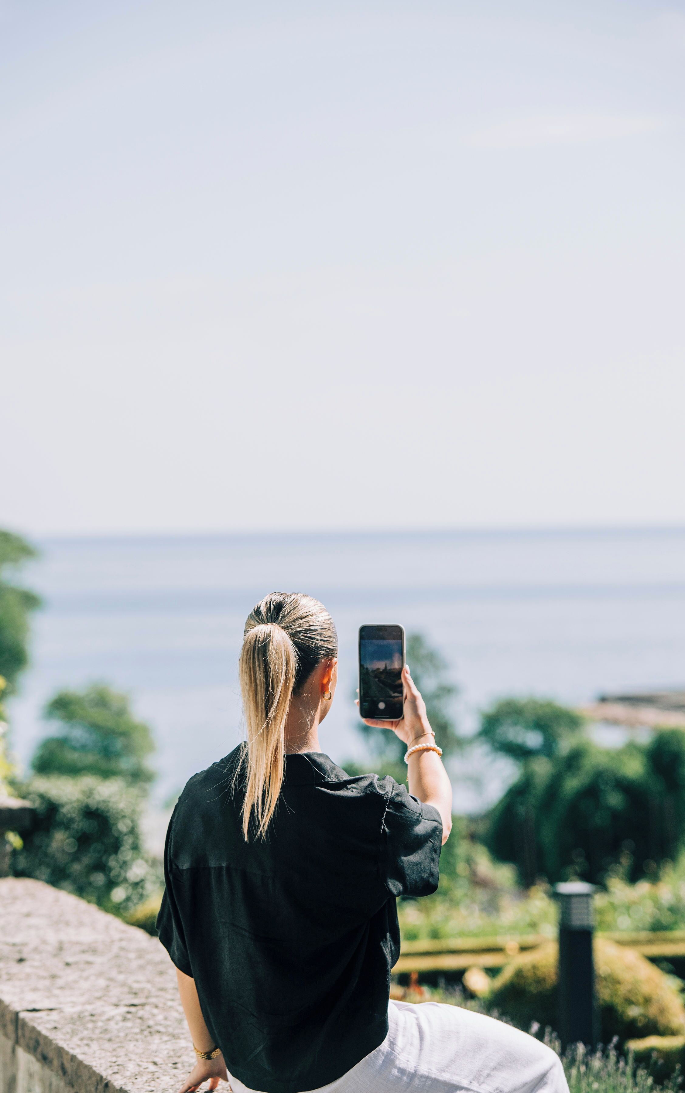 Una persona tomando una foto con un teléfono inteligente, con vista a un cuerpo de agua y vegetación.