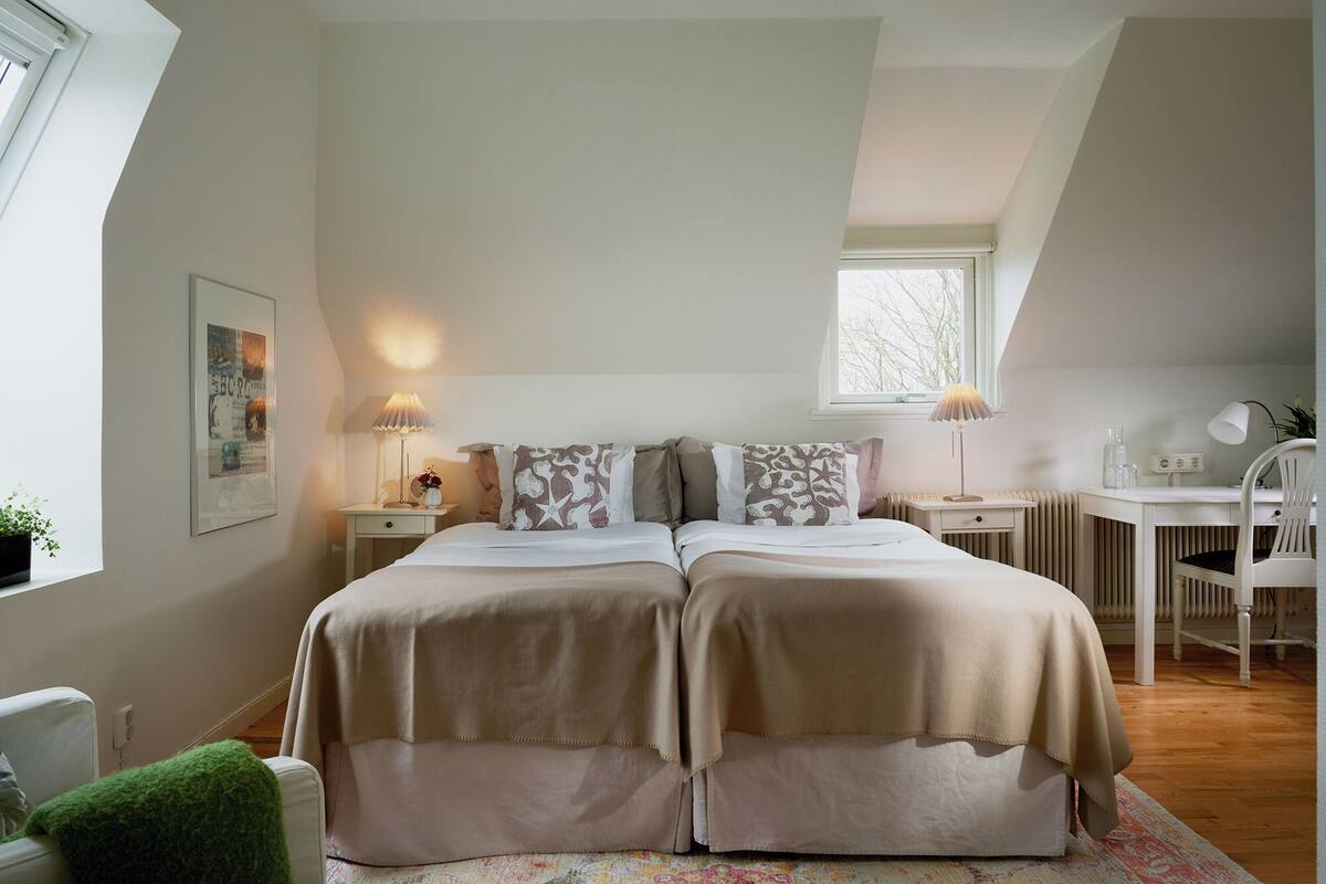 A bedroom with a double bed, two bedside tables, a desk, a chair, and a window.