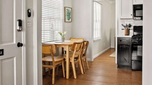 Una cocina moderna con armarios blancos, un microondas negro y una mesa de comedor de madera con sillas.
