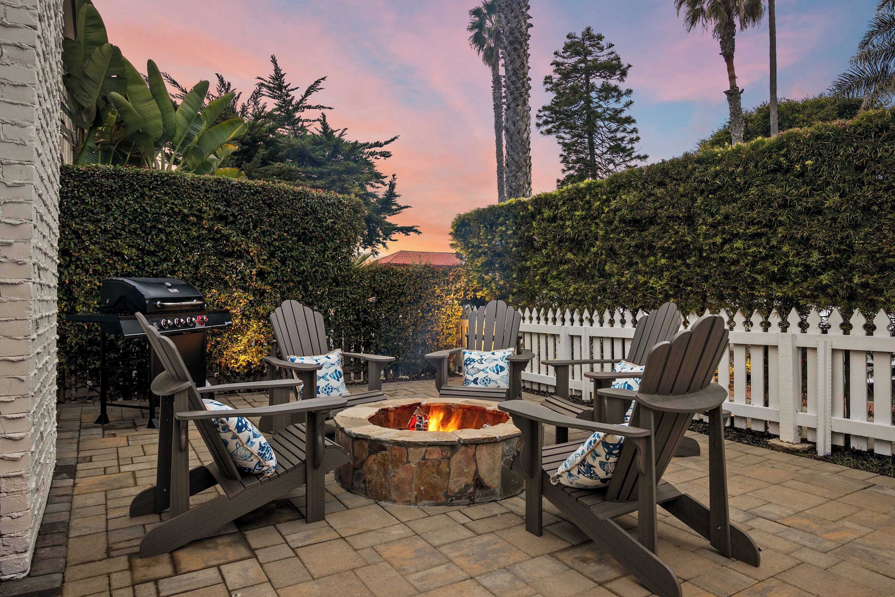 A patio with Adirondack chairs, a stone fire pit, and a grill.