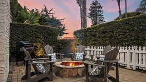 Un patio con sillas Adirondack, un hogar a leña de piedra y una parrilla.