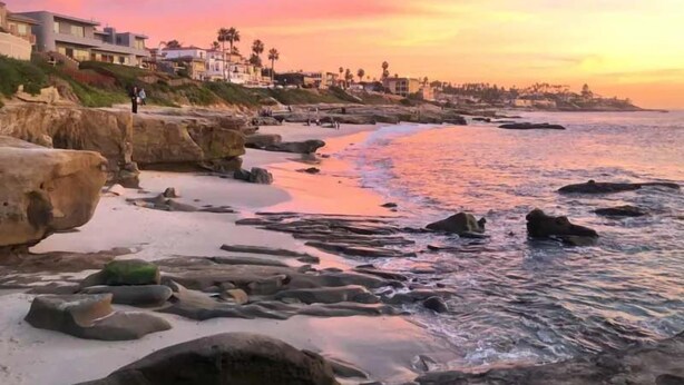 A coastal landscape with a rocky shoreline, a sandy beach, and buildings in the background. - Ocean Retreat 1BR Walk to Windansea Beach (San Diego)