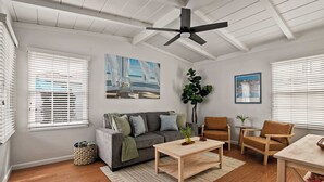 A living room with a grey sofa, a wooden coffee table, and a ceiling fan. - Ocean Retreat 1BR Walk to Windansea Beach (San Diego)