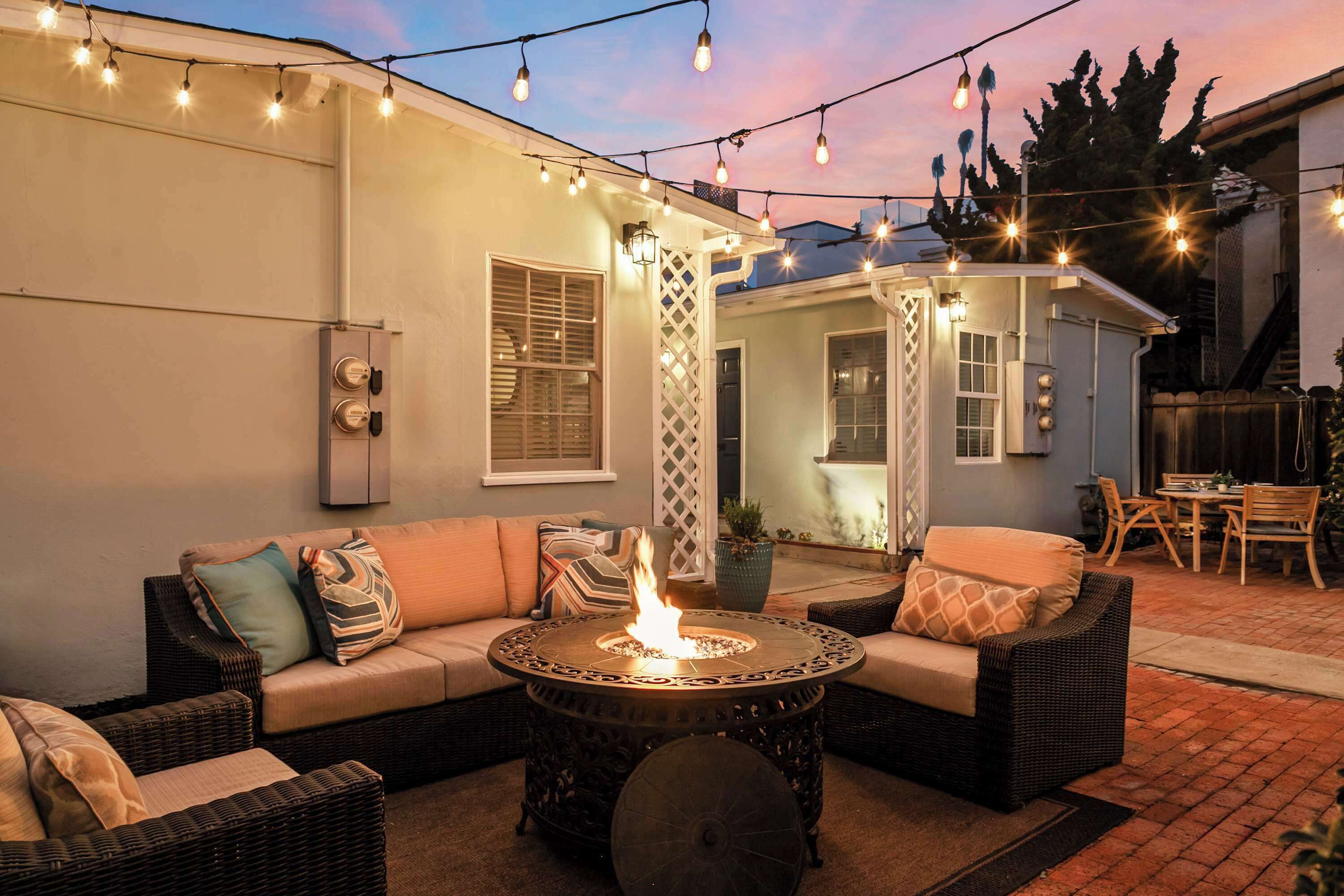 An outdoor patio with a fire pit table, wicker furniture, and string lights.