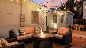An outdoor patio with a fire pit table, wicker furniture, and string lights. - Ocean Retreat 1BR Walk to Windansea Beach (San Diego)