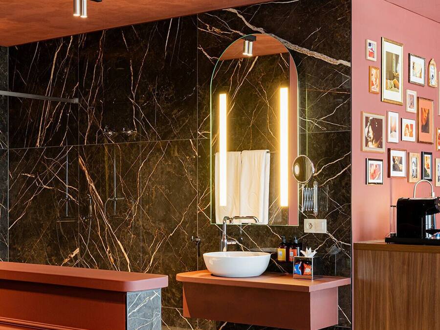 Een moderne badkamer met een marmeren wastafel, een spiegel en een wastafelmeubel met een koffieapparaat.
