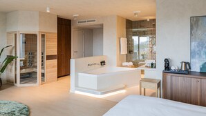 Ein modernes Schlafzimmer mit einem großen Bett, einem begehbaren Kleiderschrank, einem Badezimmer mit Glasdusche und einer Kaffeestation.